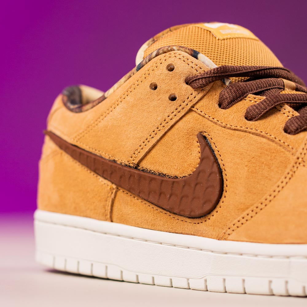 Close-up of the READ BELOW the BUTTON RAFFLE Nike SB Brew and Biscuits Dunk Low, featuring tan suede, textured brown swoosh, brown laces, and a white sole against a purple backdrop—ideal for your next Southside Skatepark raffle entry.