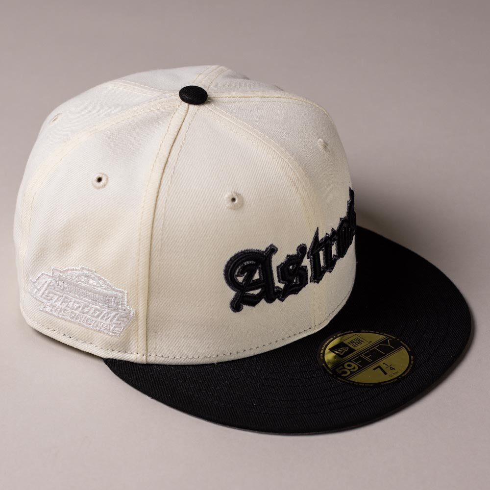 Photographed on a light surface, the Straight Outta Southside OG Chrome Black Houston Astros New Era 59FIFTY Fitted Hat features a cream and black colorway with “Houston Astros” in bold black lettering, a silver patch on the side, and a gold 59FIFTY sticker on its black brim.
