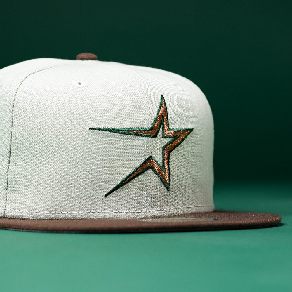 The Copper Trails OG Walnut Egreen Houston Astros New Era Hat 5950 Fitted is a white fitted cap with a brown brim, featuring an embroidered Houston Astros star logo outlined in green and orange on the front, displayed against a solid green background.