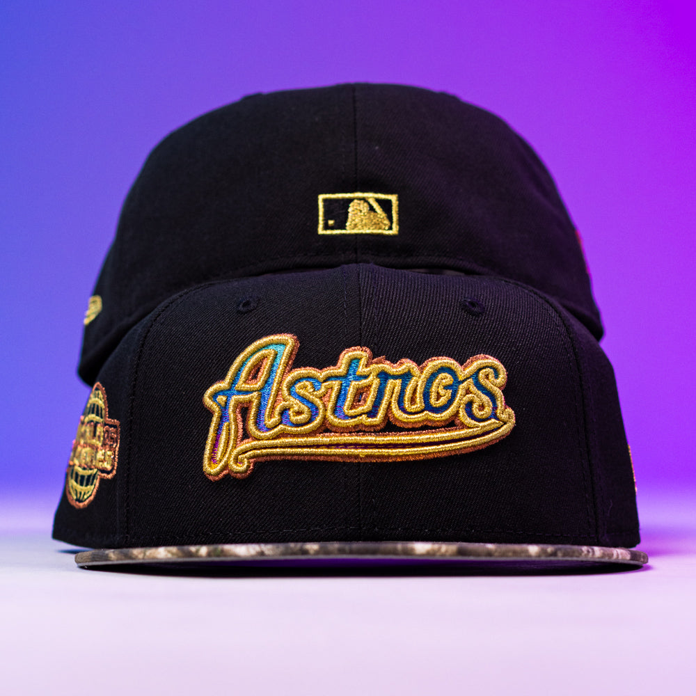Two Oil Spill WS05 Houston Astros New Era 5950 Fitted hats with gold embroidery are stacked. The top cap features "Astros" in cursive; the back shows a gold MLB logo. The background shifts from purple to blue.