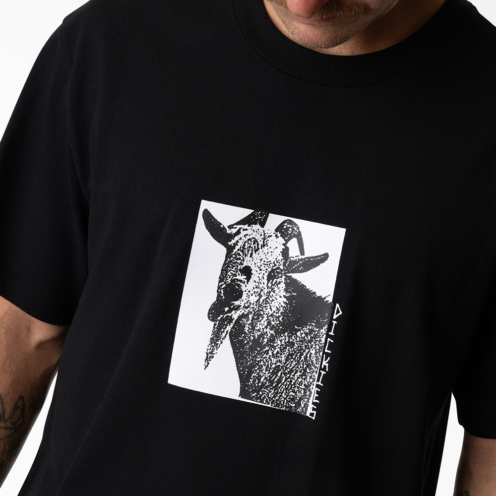 A person wears the P415867 Mike Anderson Goat Black Tee by Dickies Skateboarding, featuring a monochrome goat graphic and vertical DICKIES text; their face is partially visible.