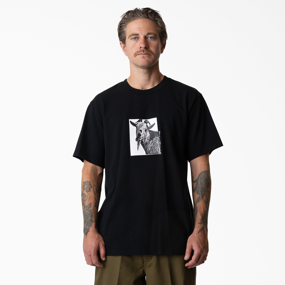 A man with tattooed arms wears the P415867 Mike Anderson Goat Black Tee from Dickies Skateboarding, standing facing forward against a plain white background.