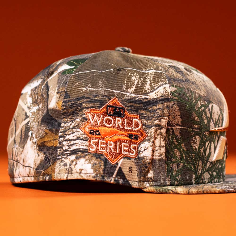 The Panhandle Real Tree Orange Houston Astros New Era 5950 Fitted hat features camo print and an orange World Series patch, displayed against an orange background.
