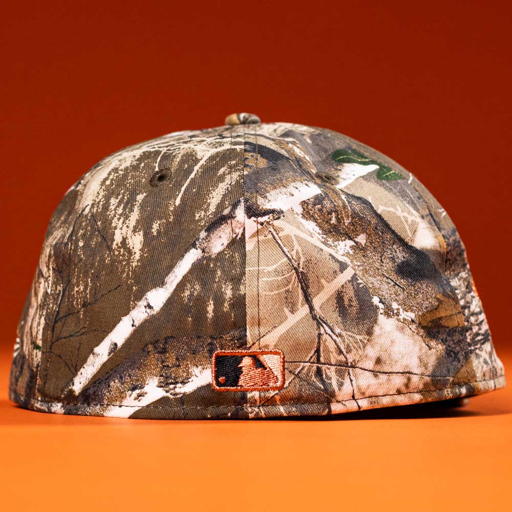 The Panhandle Real Tree Orange Houston Astros New Era 5950 Fitted Hat is shown on an orange background, displaying the back with a black, white, and orange Astros MLB logo above the brim.