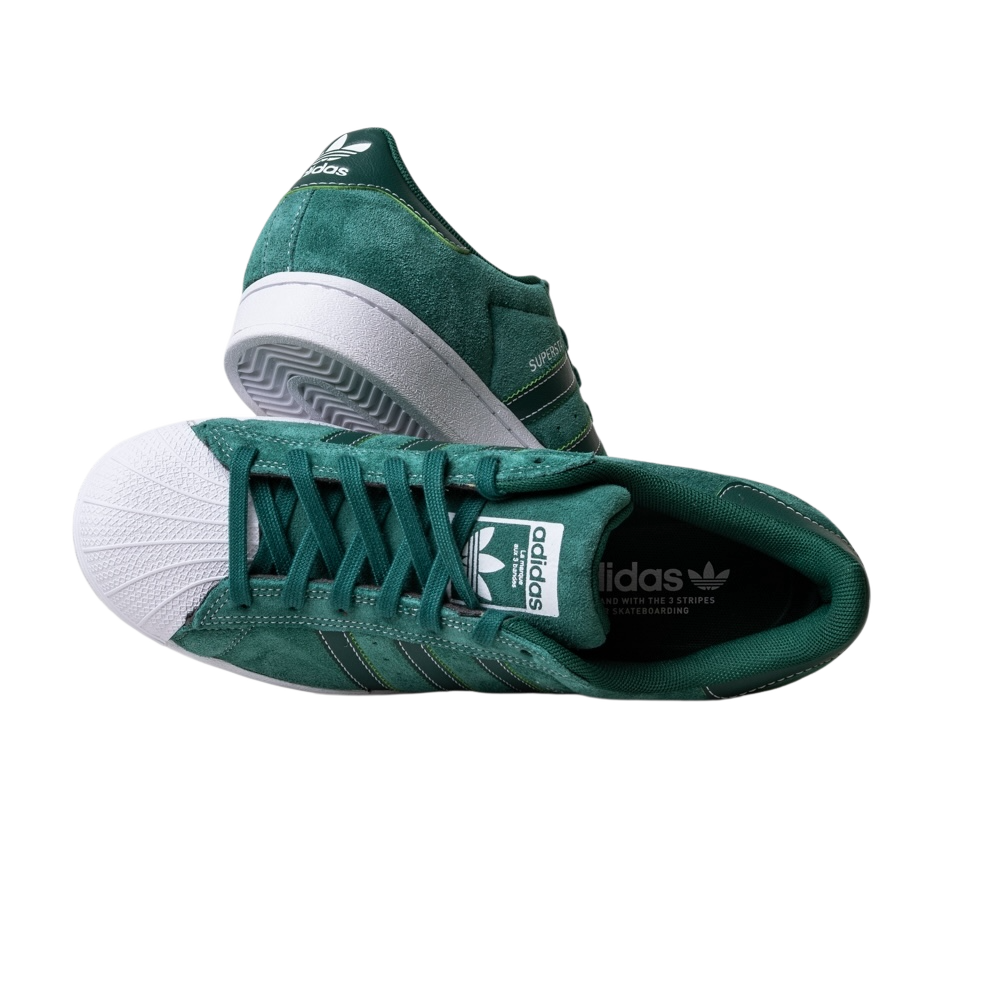 The JQ1103 Core Green White Superstar ADV Adidas Skateboarding Suede Shoes feature green suede, white shell toes, and soles. One shoe stands upright, while the other lies sideways, highlighting the Adidas logo and signature stripes.