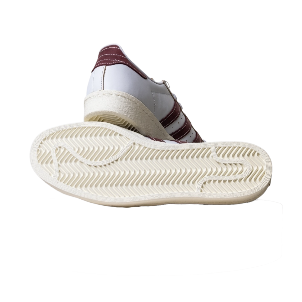 The JP8529 Cloud White Share Superstar 80 ADV Adidas Skateboarding Leather Shoes are shown, one upright and the other displaying its textured off-white zigzag sole and maroon stripes.