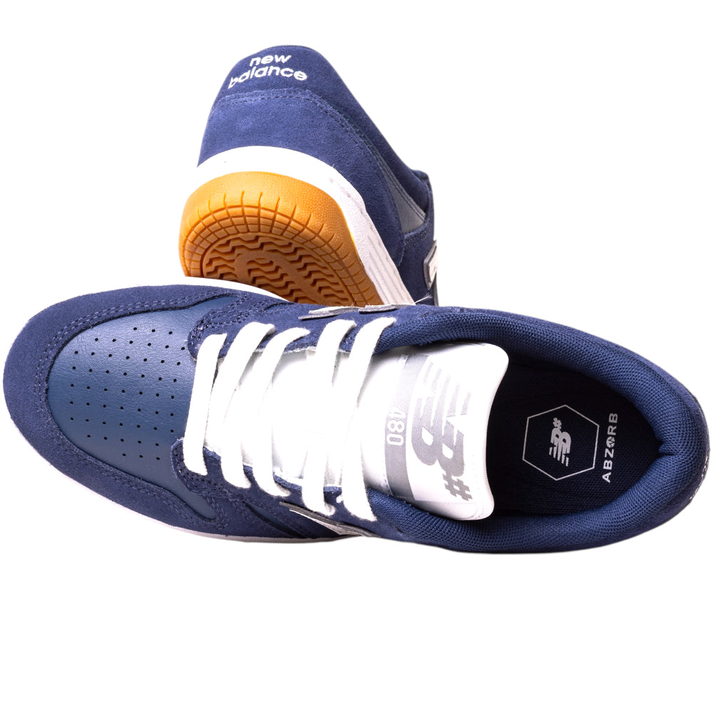 A pair of 480BEE Navy White New Balance Numeric Suede Skateboarding Shoes, featuring white laces and soles. One shoe stands upright showing the sole; the other lies flat displaying the top and insole, mixing classic and modern style.