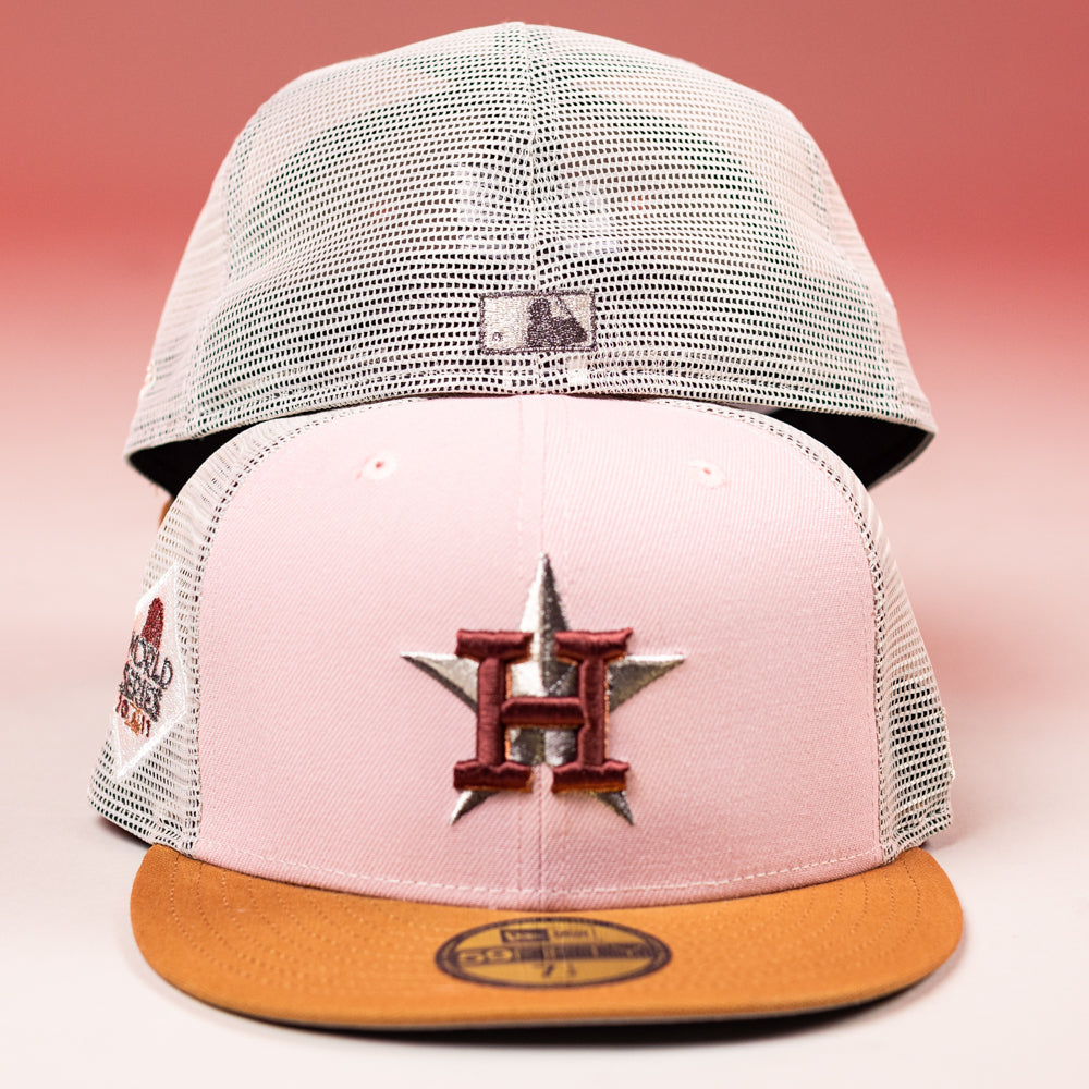 The 17WS Pink Trucker Houston Astros New Era Hat 5950 Fitted features pink and white mesh, a brown brim, an embroidered “H” star logo, and a 2022 World Series side patch, shown in front of another similar cap.