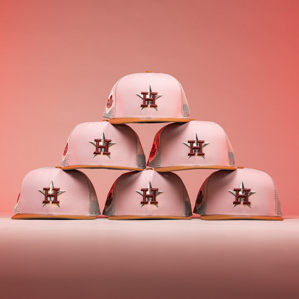 Six 17WS Pink Trucker Houston Astros New Era Hat 5950 Fitted caps are stacked in a pyramid on a pink background, each featuring the Astros’ star logo on the front.