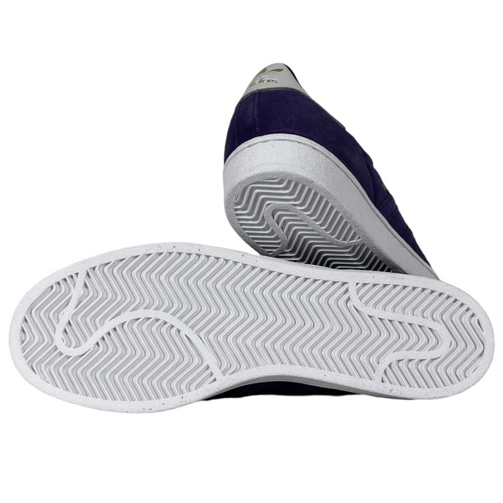 The Purple Zero Gold Superstar ADV Adidas Skateboarding shoes feature a dark suede upper, subtle reflective badging, and white rubber soles with a zigzag tread pattern, shown from the side and bottom.