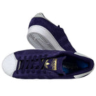 A pair of Purple Zero Gold Superstar ADV Adidas Skateboarding suede shoes with white shell toes, reflective badging, and logo. One shoe is upright showing laces; the other lies sideways, revealing the sole and design features.