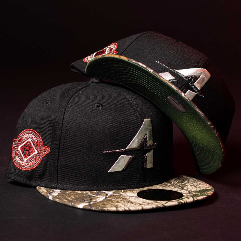 Two black Red Dot Red City Connect Houston Astros New Era 5950 fitted hats with camo brims, silver A logos, and circular patches are displayed. Pre-order now for in-store pick-up or quick fulfillment.