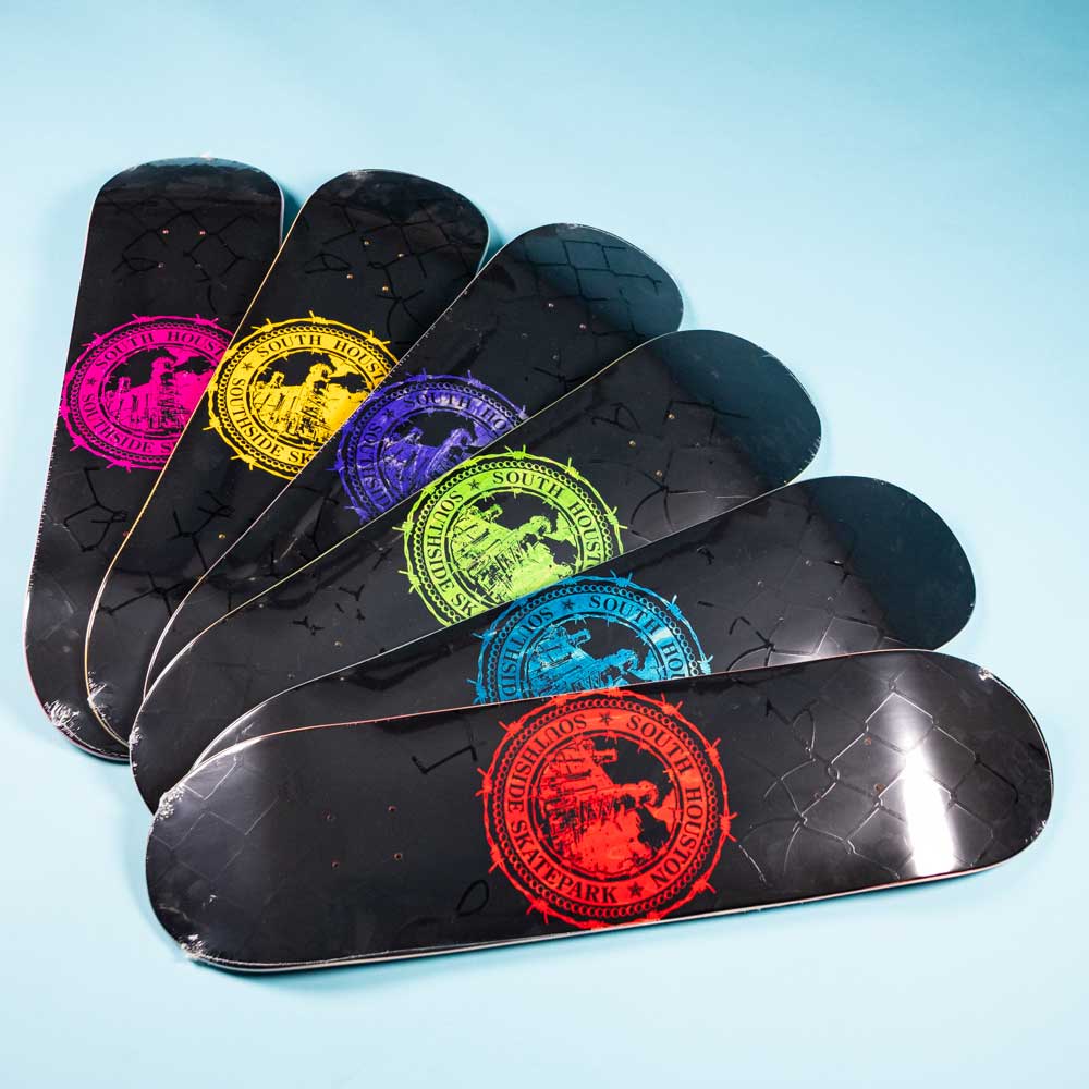 Six black Refinery Southside Skateboard Decks by Bigo are arranged fan-style on a light blue surface, each featuring a colorful South Park graphic and stained veneer icon, inspired by Southside Skatepark’s bold creativity.