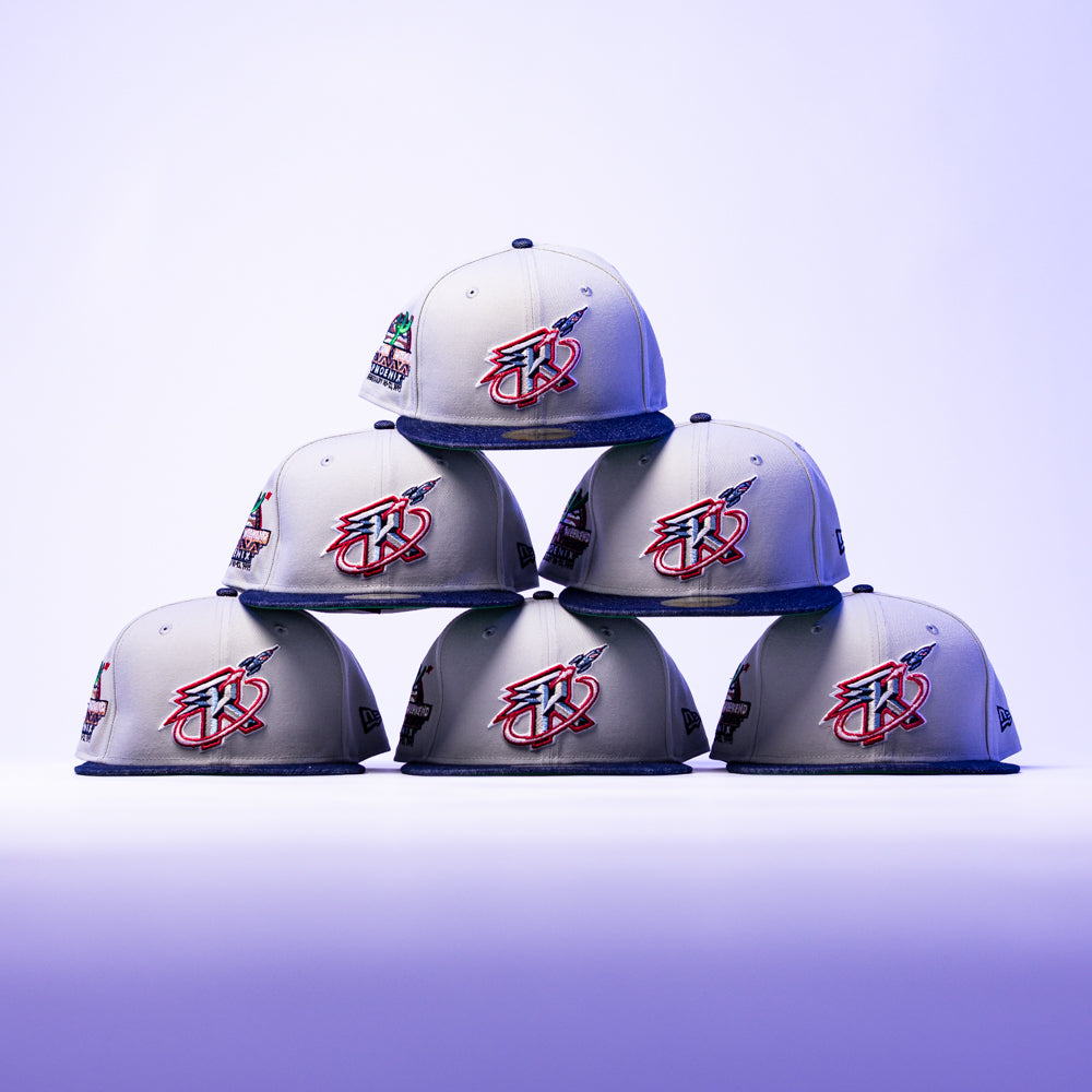 Six grey The Unit 95 ASG Denim Houston Rockets New Era Hat 5950 Fitted caps with vibrant embroidered logos are stacked in a pyramid against a purple gradient backdrop, highlighting their iconic style.