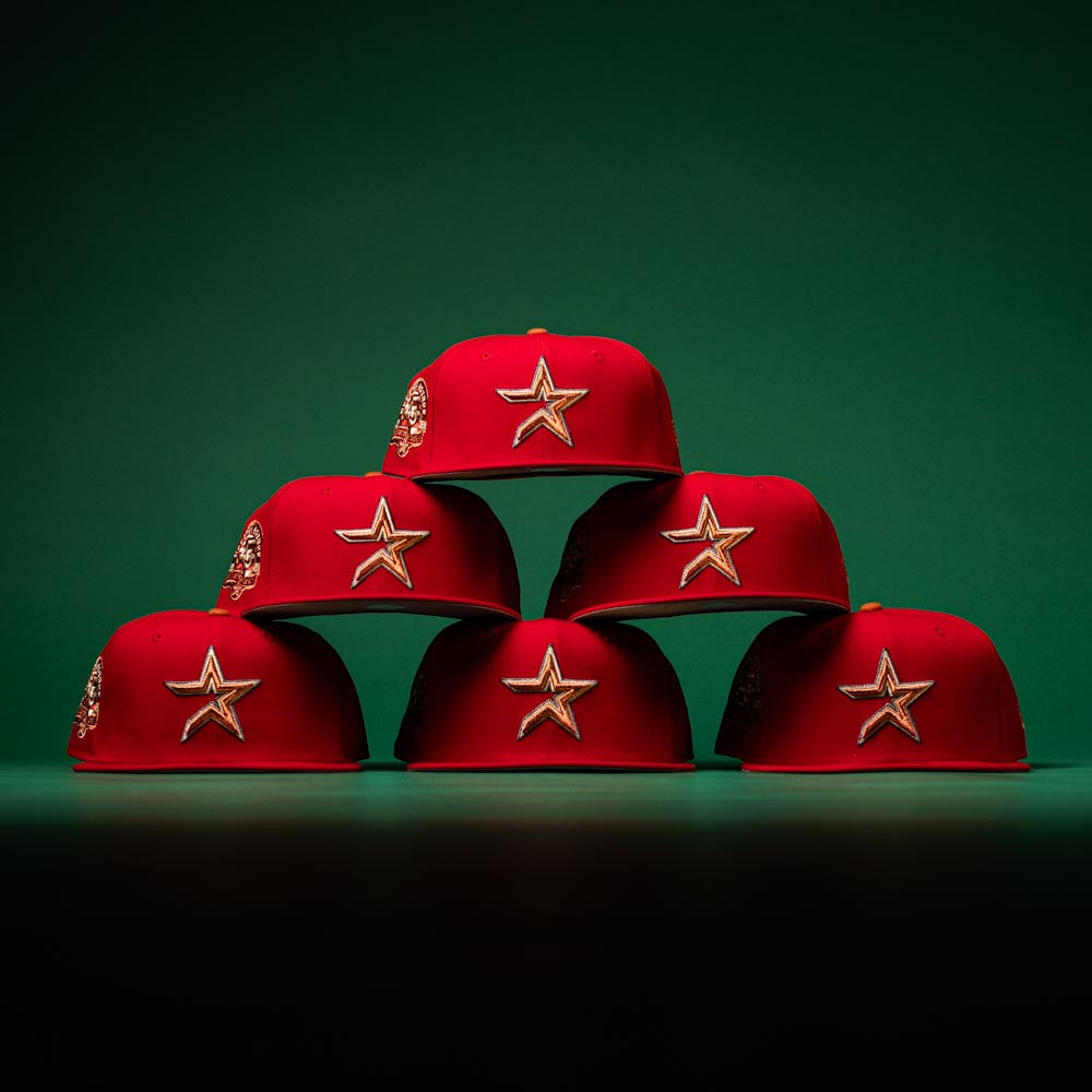 Six Rusty Screw OG Scarlet Copper Houston Astros New Era 5950 Fitted hats are stacked in a pyramid shape against a dark green background. Each hat features the classic New Era design, adding a touch of timeless style to this striking arrangement.