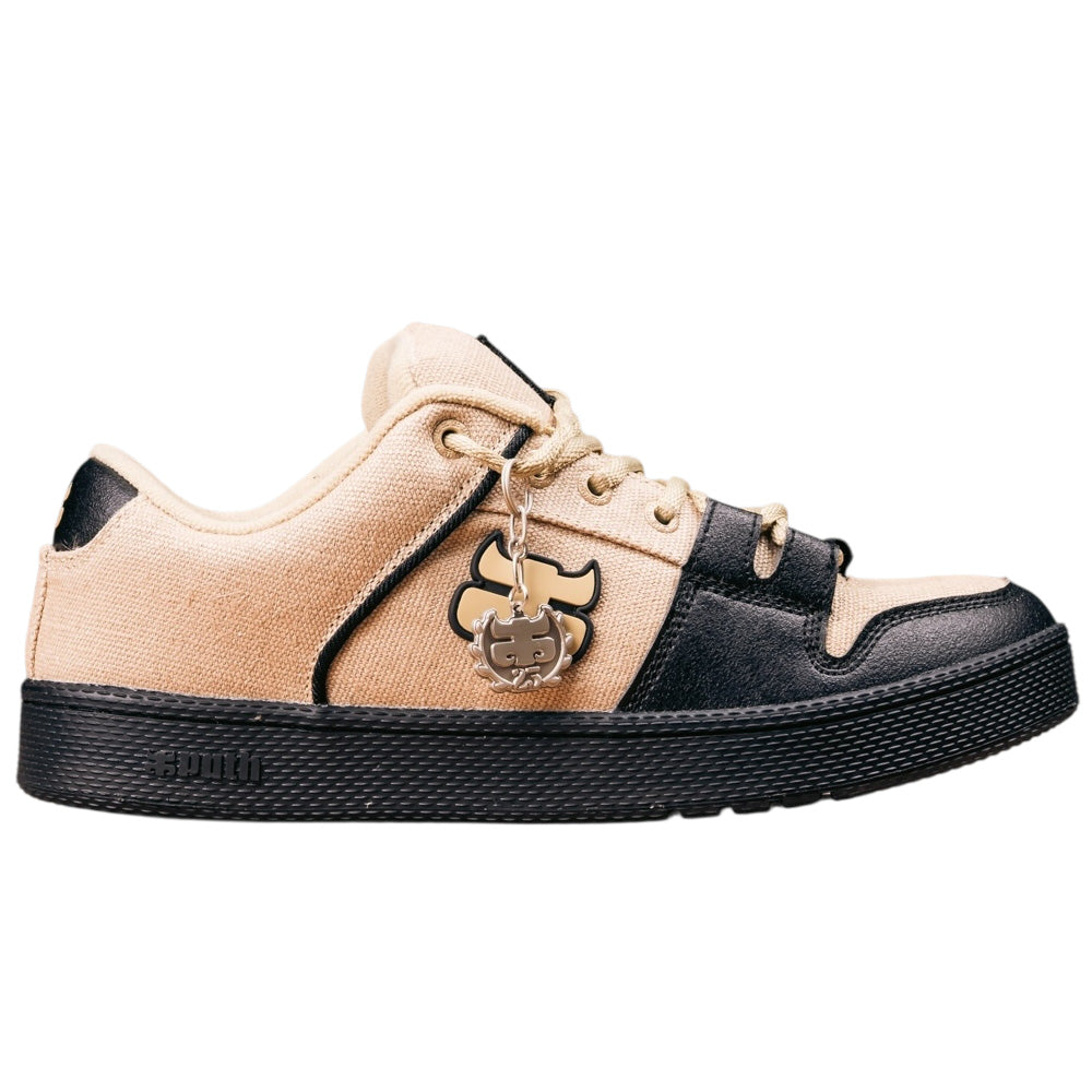 The Cricket Natural Hemp I Path Shoes Skateboarding are beige and black low-top sneakers with a black cupsole, canvas and leather-like materials, contrast stitching, and a metallic bear-shaped keychain on the laces.