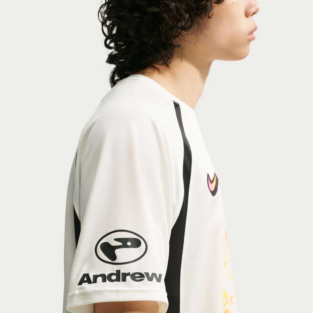 A person with curly hair, shown from the side, wears a Nike SB Sail Black IR6760133 Skate Jersey with black accents and Andrew's snake logo on the sleeve. The imported polyester body is designed for easy machine washing.