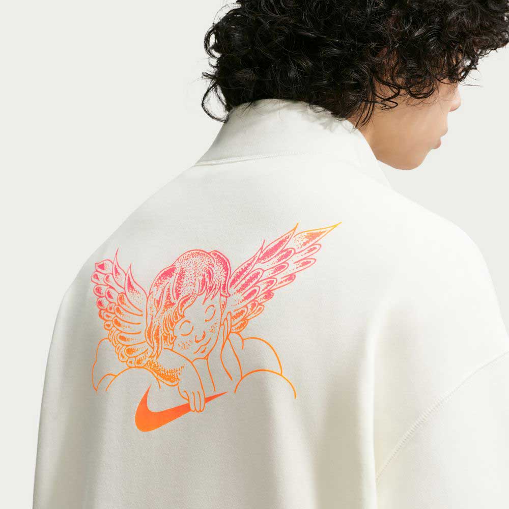 A person with curly hair wears the white Nike SB Skateboarding Sail IM5463133 1/2 Zip Fleece Crew, featuring a pink and orange sleeping angel illustration with wings and a Nike swoosh on the back; machine washable for easy care.