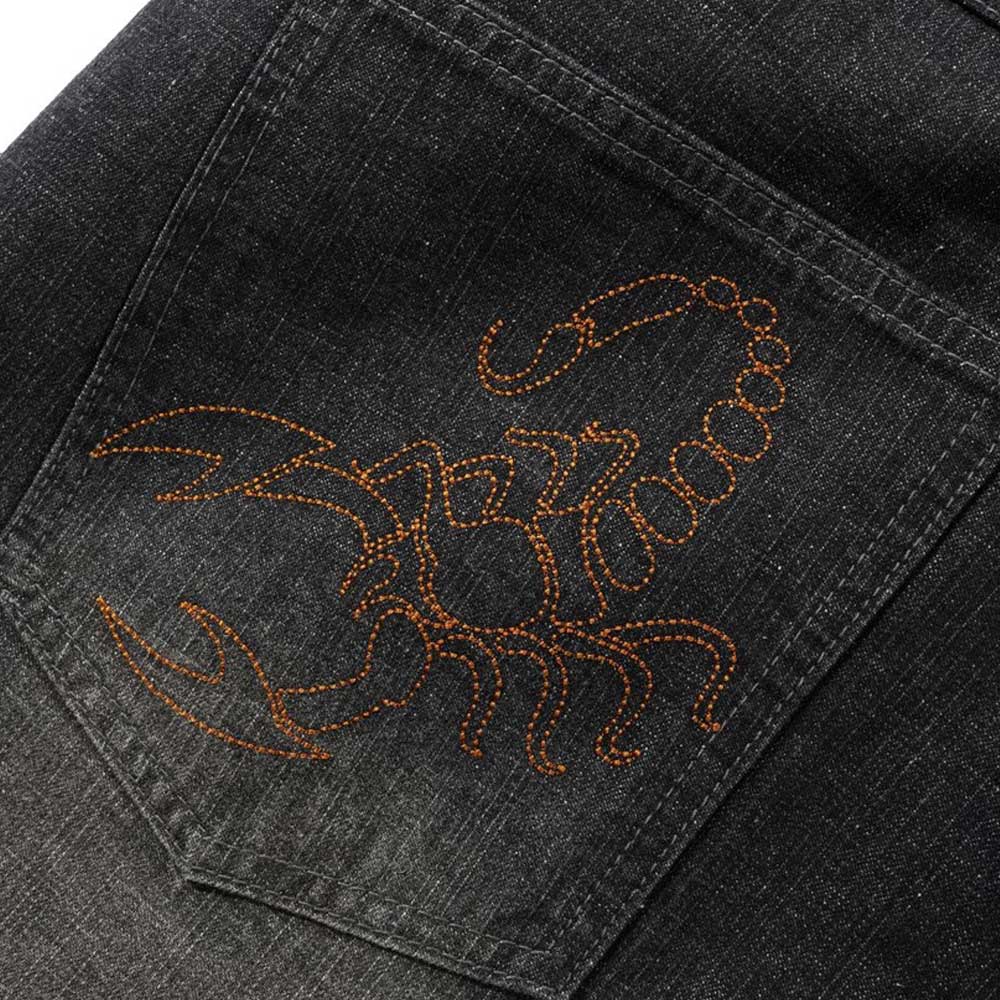 Close-up of a back pocket on the Distressed Flat Black Relaxed Denim Jeans by Butter Goods, featuring an orange-stitched scorpion outline, crafted from 100% cotton in a relaxed fit.
