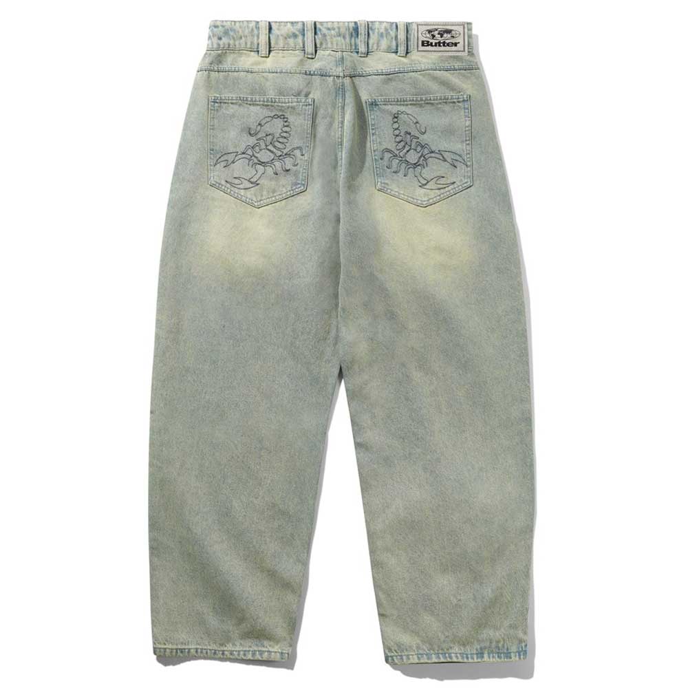Scorpion Stitch Tinted Light Blue Denim Jeans by Butter Goods feature a baggy fit, wide legs, embroidered scorpion designs on the back patch pockets, and a rectangular Butter Goods label on the waistband.