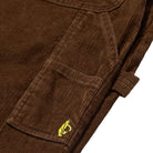 Close-up of the Shmoo Carpenter Brown Corduroy Krooked Pant pocket, showcasing a yellow embroidered penguin logo on the flap and highlighting the textured brown corduroy fabric and detailed stitching.