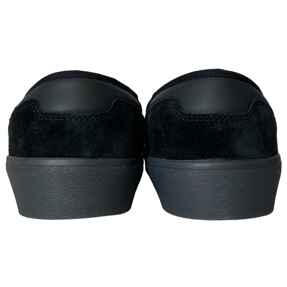 A pair of Shmoofoil Slip Adidas Skateboarding Core Black Carbon Suede Shoes, viewed from the back, displays textured rubber soles and low-profile heels against a white background.