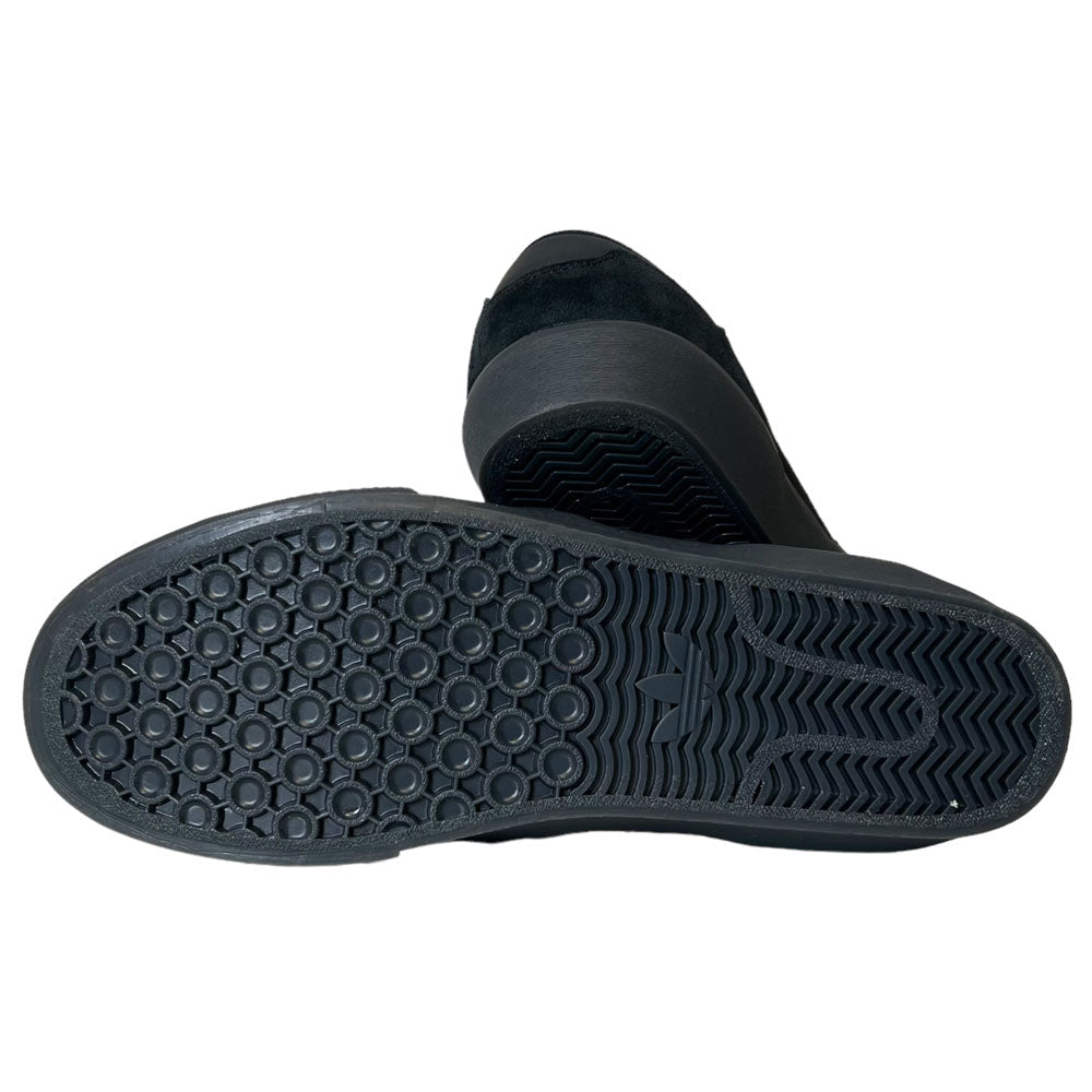 A close-up of the black rubber soles on Shmoofoil Slip Adidas Skateboarding Core Black Carbon Suede Shoes, highlighting their hexagonal and wavy tread pattern for improved grip and traction.