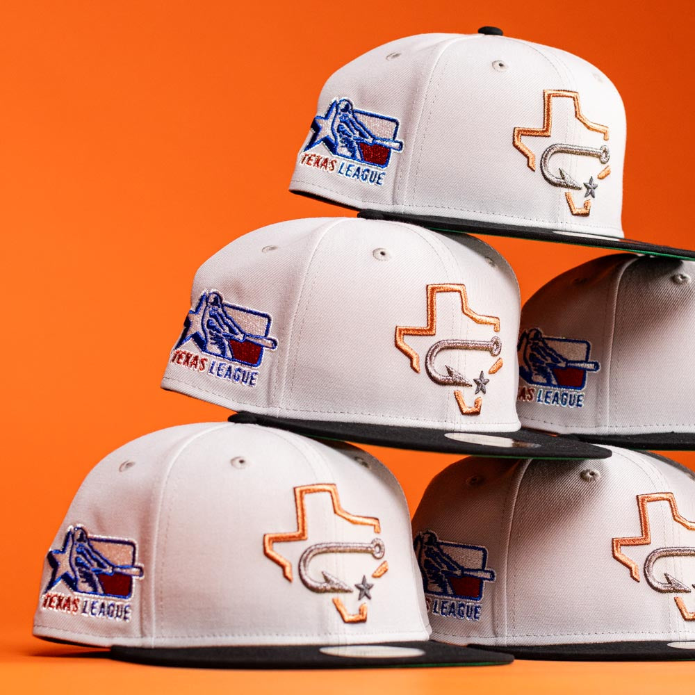Six Backlash Corpus Christi Hooks New Era 5950 Fitted hats in white are stacked against an orange background, each featuring a Texas outline with a star and bat, plus an embroidered Texas League logo on the side.