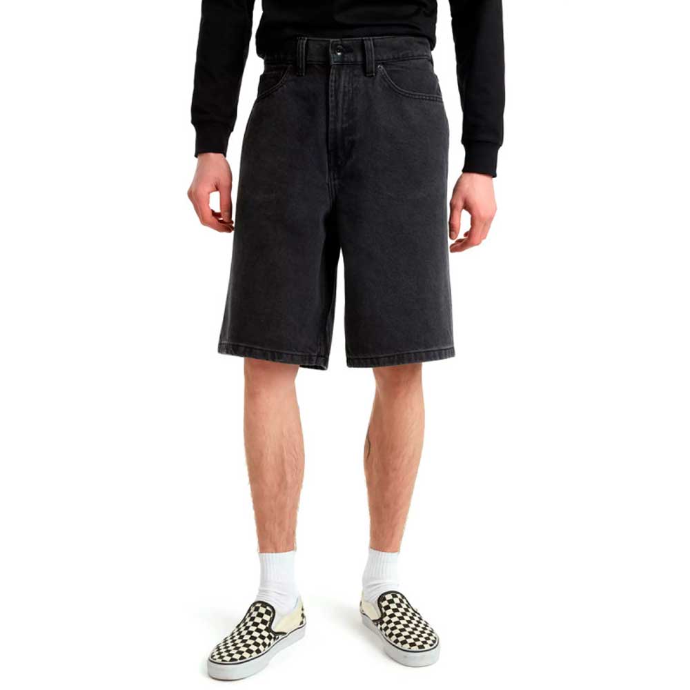 A person wearing a black long-sleeve shirt, Skate Check 5 Loose Shorts Black Denim Vans Skateboarding, white socks, and black-and-white checkered slip-on shoes stands against a white background.