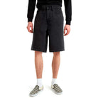 A person wearing a black long-sleeve shirt, Skate Check 5 Loose Shorts Black Denim Vans Skateboarding, white socks, and black-and-white checkered slip-on shoes stands against a white background.