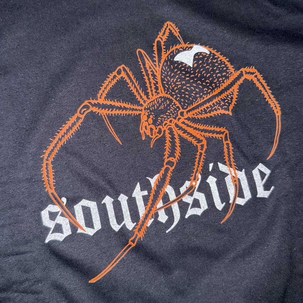 The Southside Tee Spider Black Orange Reflective features an orange spider with a white mark above bold, gothic-style “southside” lettering on dark 100% USA cotton—streetwear style.