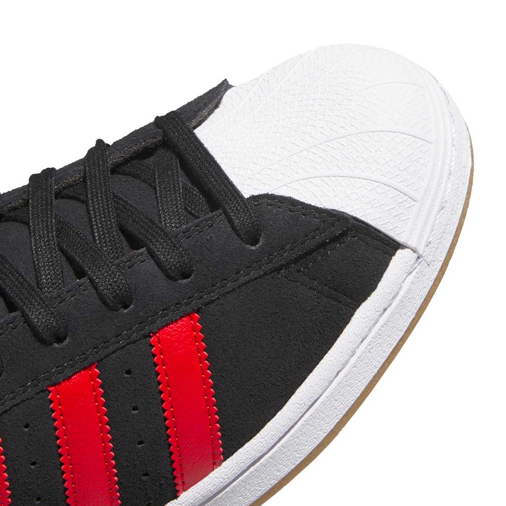 A close-up of the adidas Superstar ADV Black Red KI5731 Skateboarding Shoes highlights their red stripes, black laces, white textured rubber toe cap, and durable suede leather design with visible stitching details.