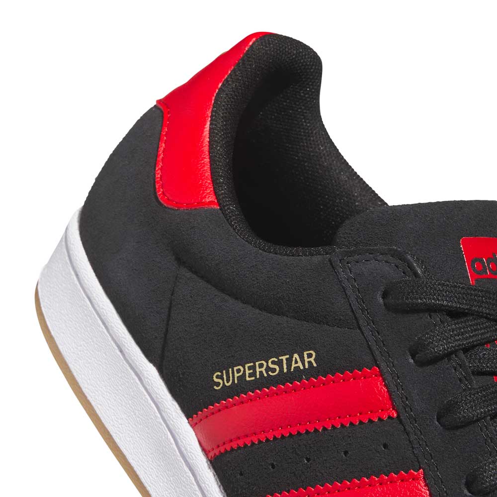 Close-up of the adidas Superstar ADV Black Red KI5731 Skateboarding Shoes, featuring red stripes and heel, white sole, suede leather upper, and gold SUPERSTAR lettering—ideal trainers for skateboarding.