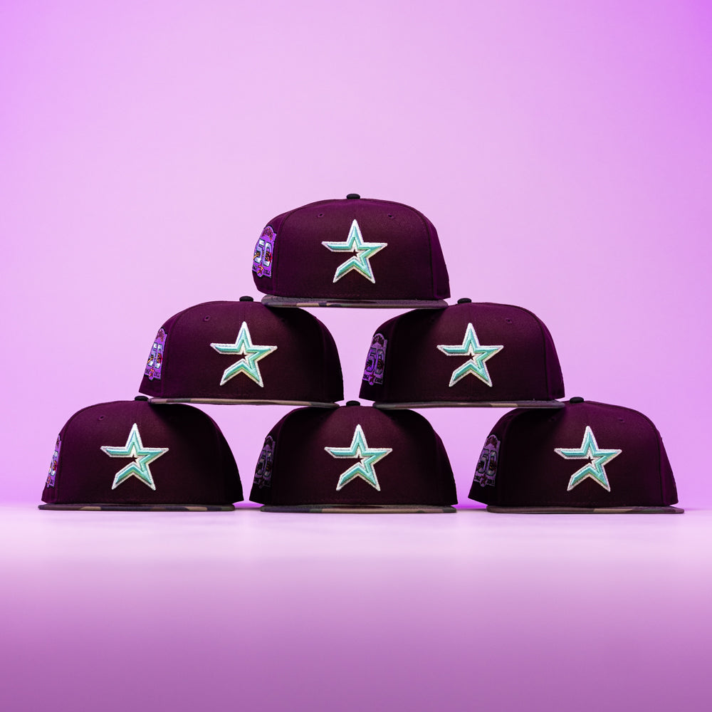 Six Swag Era 50th Camo Maroon Houston Astros New Era Hat 5950 Fitted caps are stacked in a pyramid against a pink and purple gradient background.