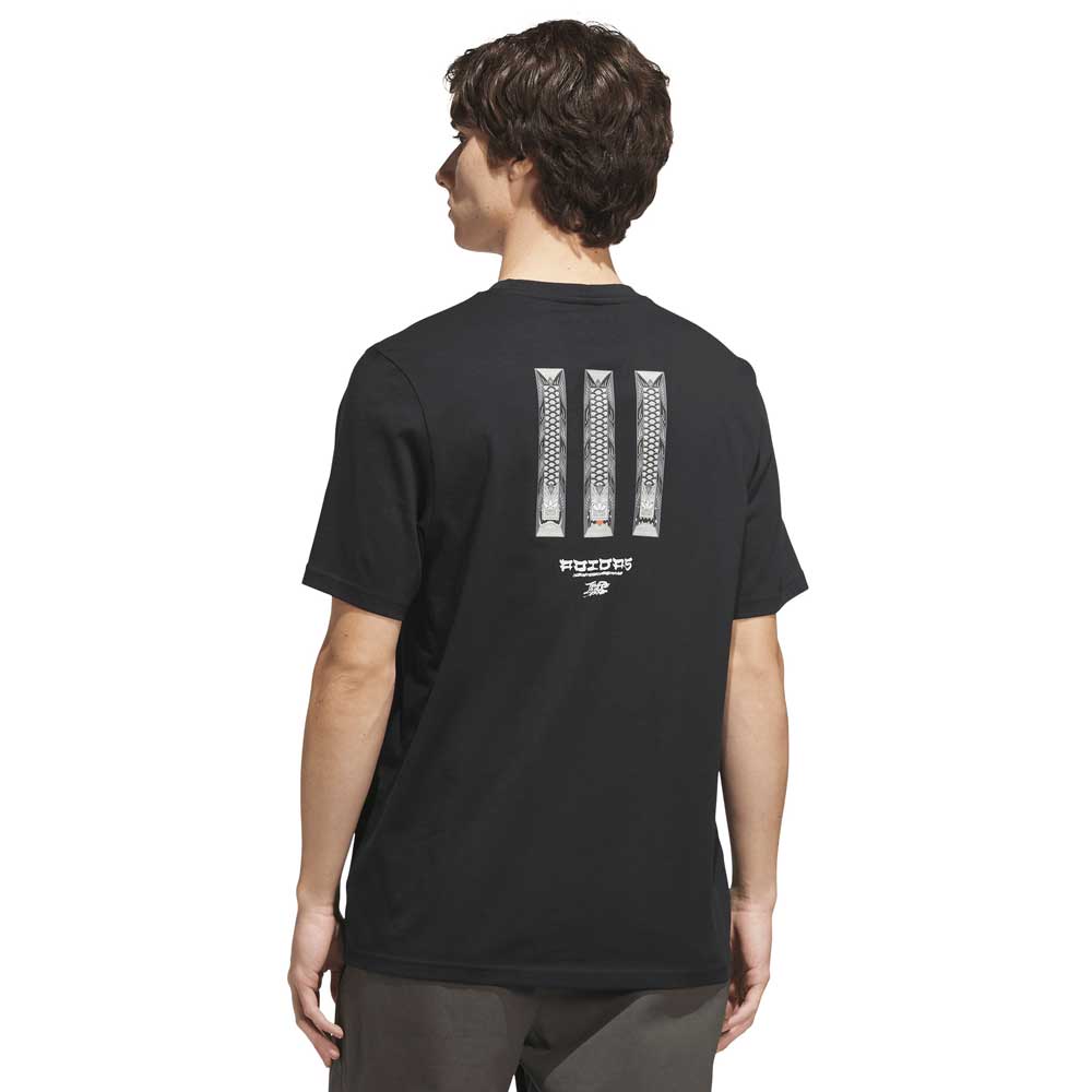 A person wearing the adidas Skateboarding TOS Curb Tee Black Multi (style KS4338), featuring three vertical, patterned stripes and small white text on the back. The individual stands with their back to the camera, capturing classic skate culture style.