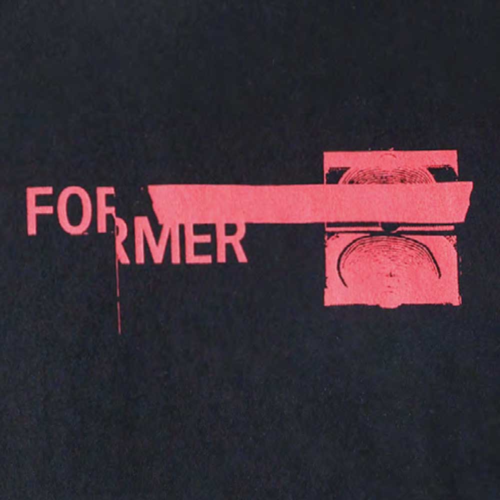 The Tape Crux Former Tee Black features the word FORMER in pink, partially covered by a pink bar beside an abstract pink circular pattern—all set against a black background. This bold design recalls the vintage style and classic screen print of timeless t-shirts.