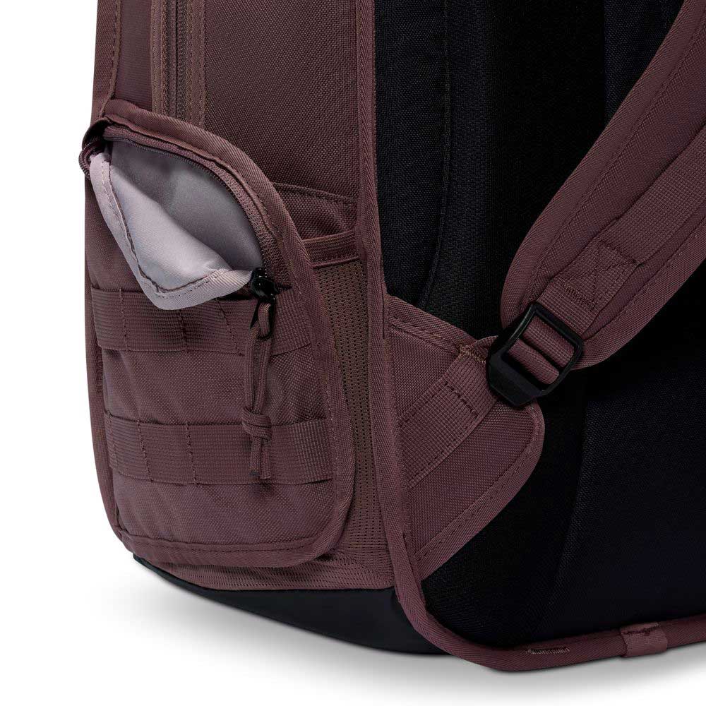 Close-up of the Tattoo Black Light Violet FD7544502 Nike SB RPM Skate Backpack showing a partially open water-resistant side pocket with zipper, padded shoulder strap, black back panel, light gray interior, and webbing detail.