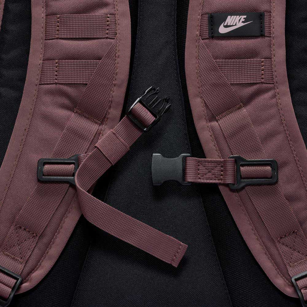 Close-up of the maroon shoulder straps on the Tattoo Black Light Violet FD7544502 Nike SB RPM Skate Backpack, featuring a black Nike logo patch and center buckle fastener, set against a black background.