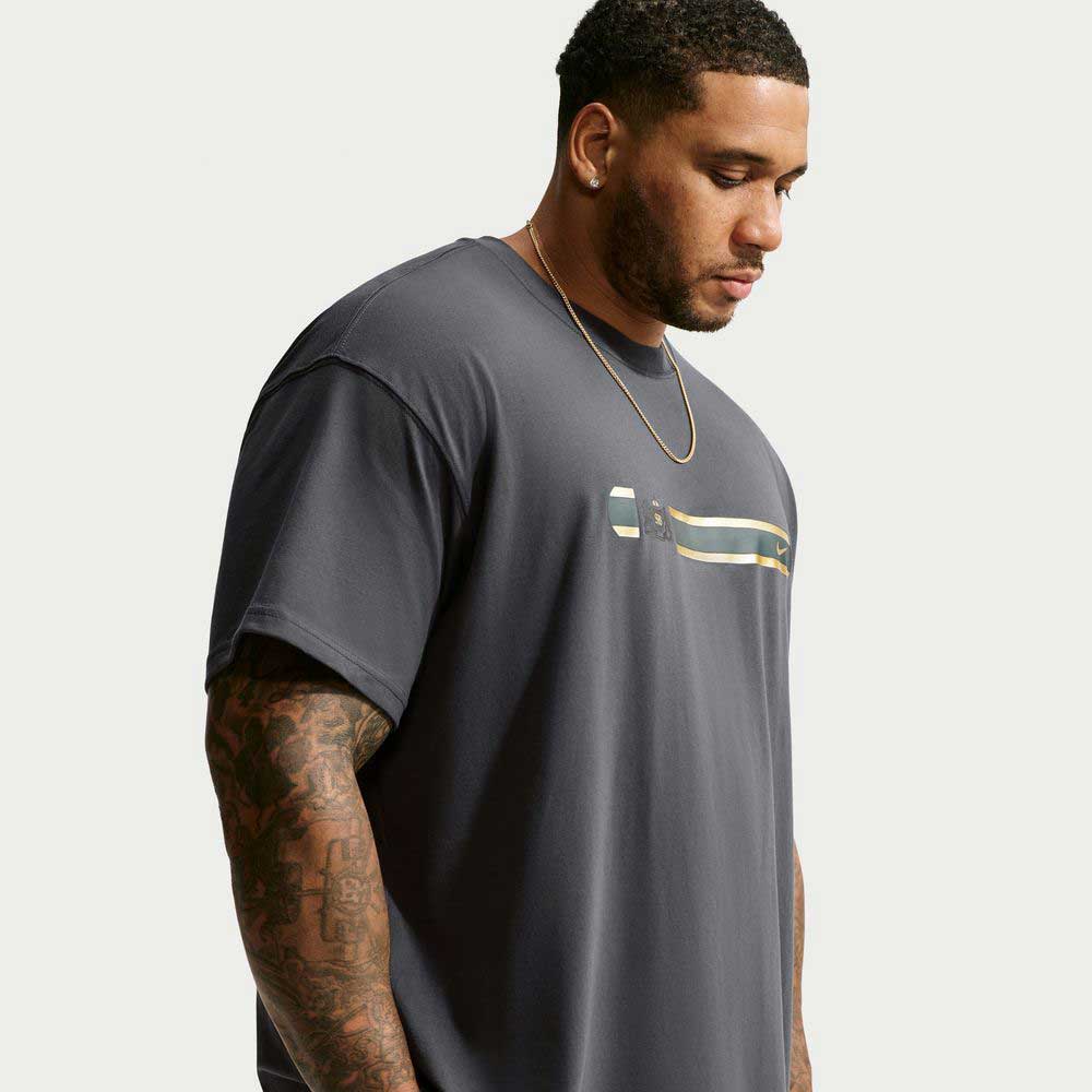 A man wearing a black Tee Black IW3134060 T-Shirt Nike SB Skateboarding featuring a gold and green graphic on the chest.