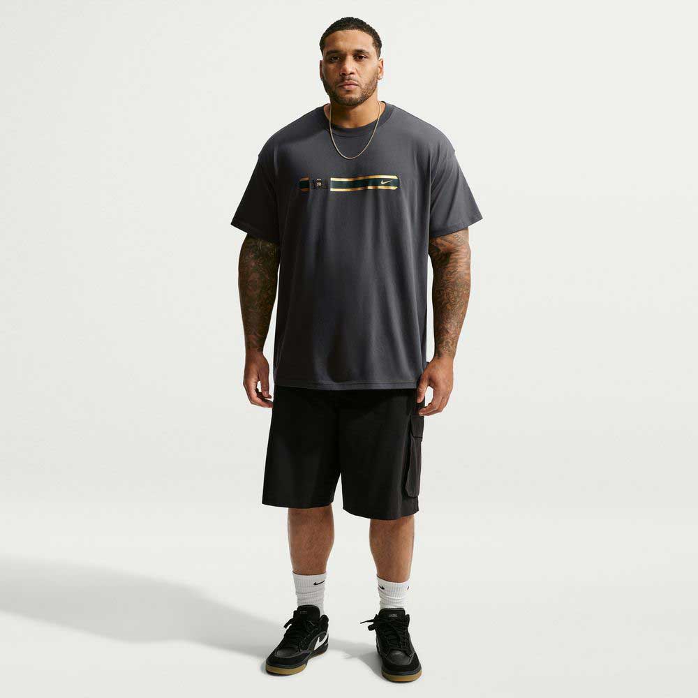 A man wearing a black Tee Black IW3134060 T-Shirt Nike SB Skateboarding with a small horizontal graphic on the chest, paired with black cargo shorts, white socks, and black sneakers.