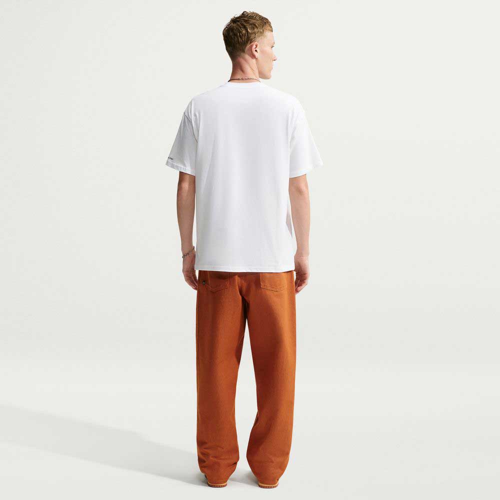 Back view of a person wearing a white Tee White IW3134100 T-Shirt Nike SB Skateboarding and loose-fitting orange trousers.