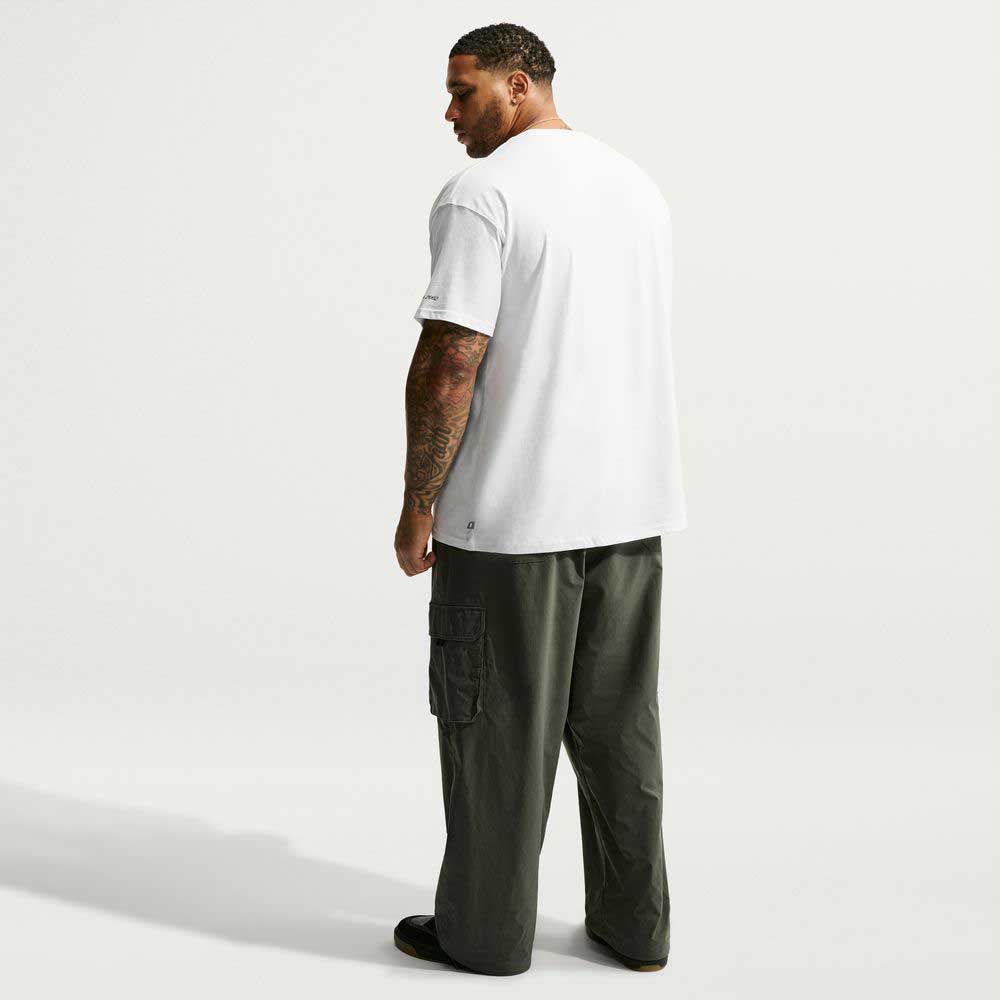 A person from behind wearing a white Nike SB Tee White IW3134100 T-Shirt Nike SB Skateboarding and baggy olive green cargo pants.