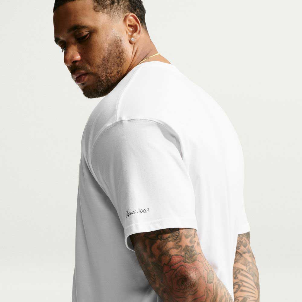 A man wearing a white Tee White IW3134100 T-Shirt Nike SB Skateboarding with small black text printed on the sleeve that reads depuis 2002.