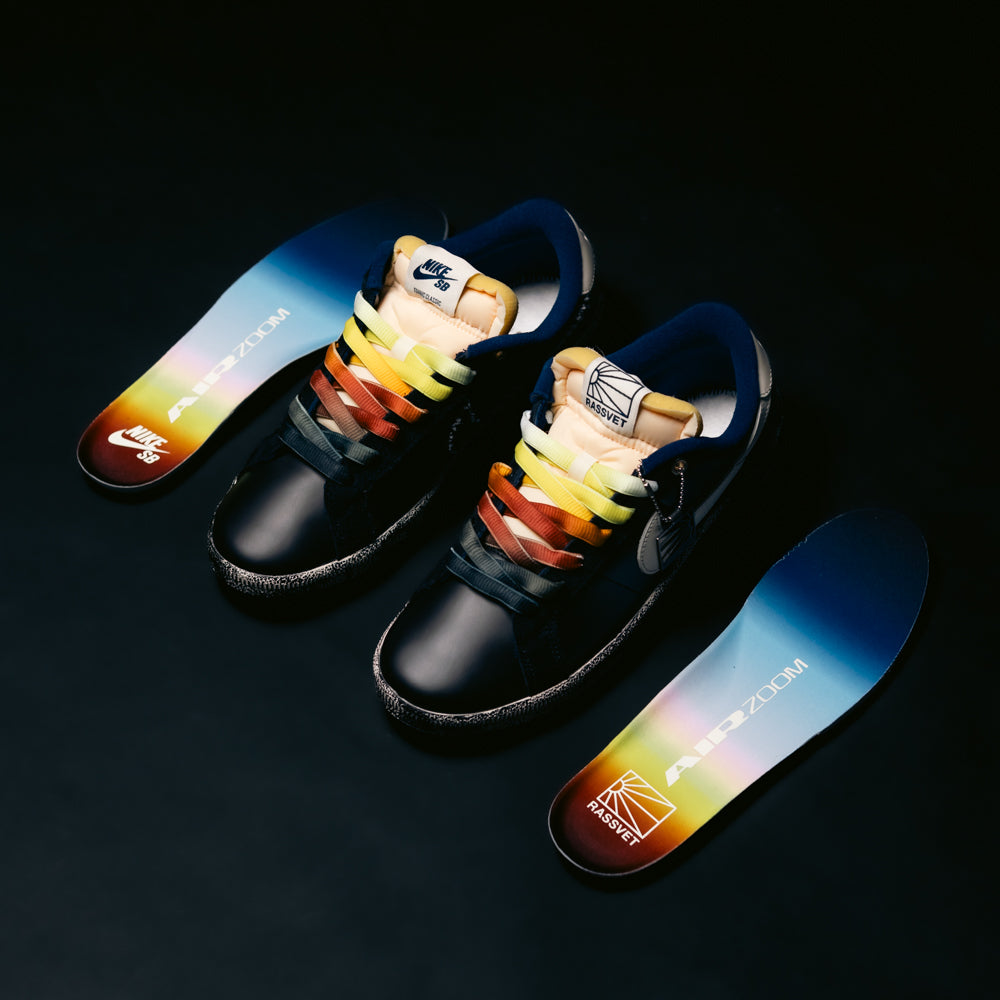 A pair of Zoom Tennis Classic x Rassvet IO9846400 Blue Void Sail Nike SB leather skateboarding shoes with colorful gradient laces and matching insoles that display a blue, yellow, and red ombre design, set against a dark background. Featuring a comfortable Solarsoft insole for enhanced cushioning.