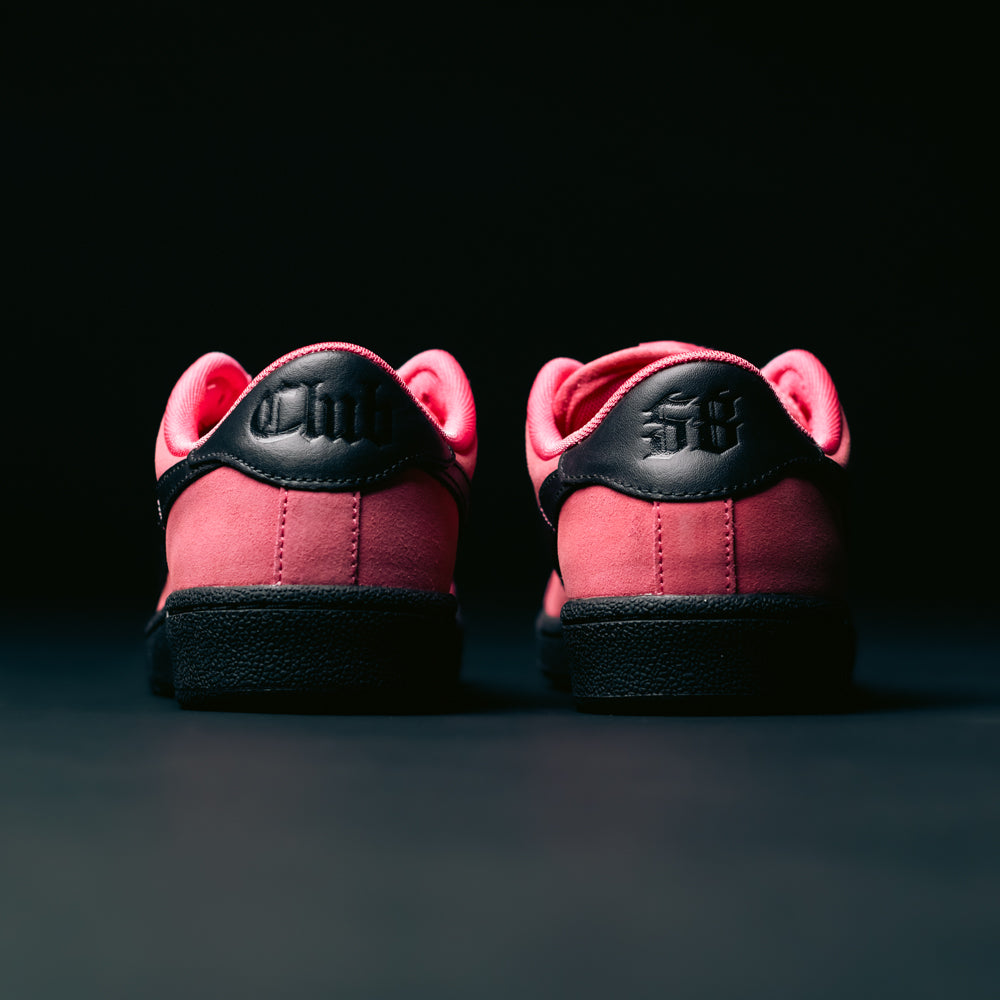 A pair of Zoom Tennis Classic IO8394600 Hyper Pink Black Nike SB Leather Skateboarding Shoes are viewed from the back, placed side by side against a dark background. The heels feature embossed black text or numbers, echoing the signature style of the Nike SB Tennis Classic.