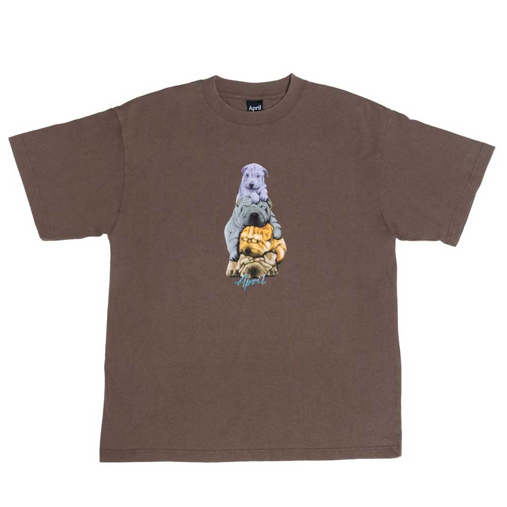 The Dogs Tee Washed Brown April Skateboards T-Shirt is a heavyweight brown tee with a unique garment-dyed look, featuring a graphic of a purple dog, gray dog, and yellow cat stacked above blue text.