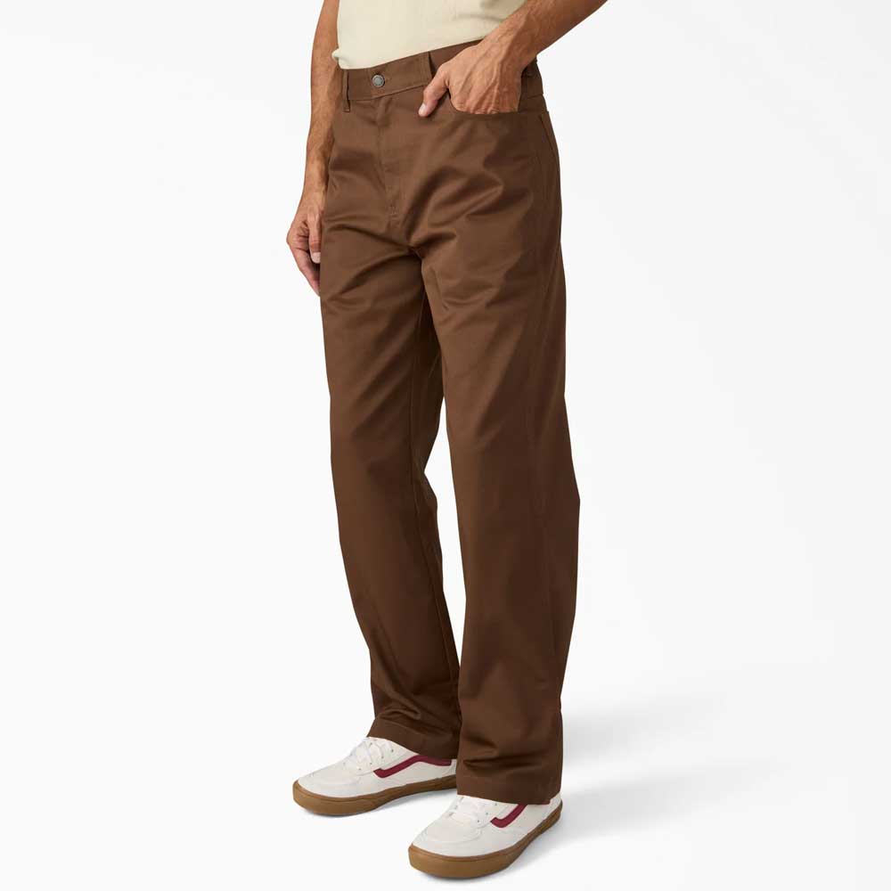 A person wears Timber Brown Union Straight Twill Pant A88580TB Dickies Skateboarding and white sneakers with red accents, standing against a plain white background. Only the lower half of their body is visible.
