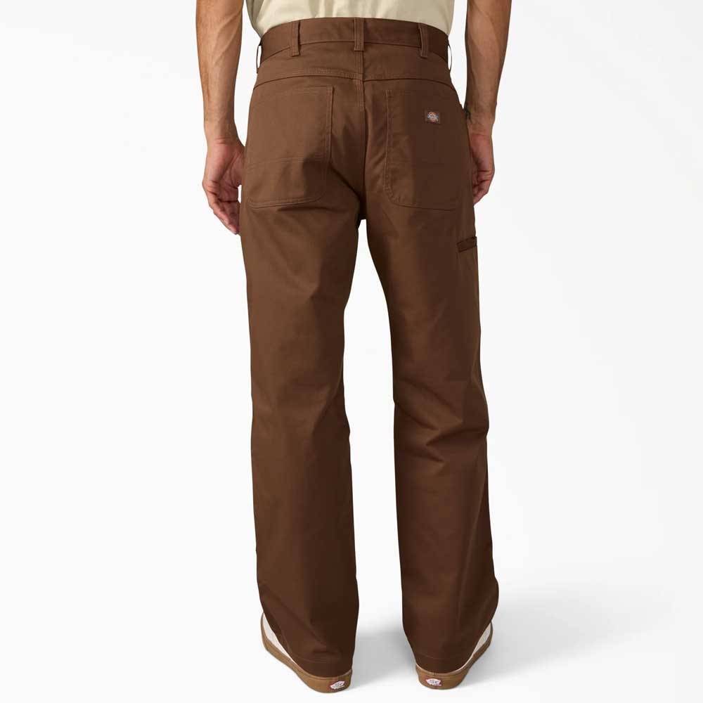 A person faces away, wearing Timber Brown Union Straight Twill Pant A88580TB from Dickies Skateboarding with visible back pockets and a logo patch above the right one, styled with casual shoes for a relaxed look.