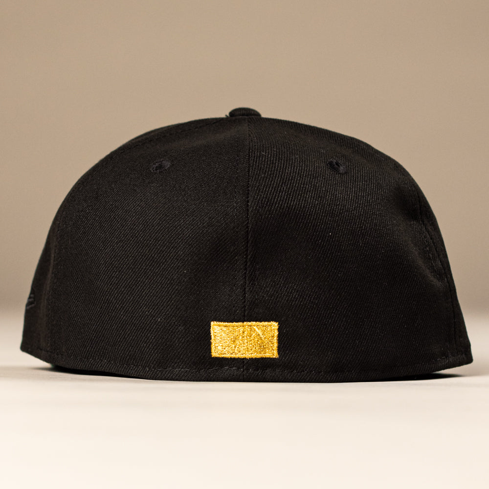 The La Morenita Black 45th Houston Astros New Era Hat 5950 Fitted by New Era is shown from the back, displaying a small gold patch near the bottom on a plain beige background—ideal for Astros fans seeking a sleek style.