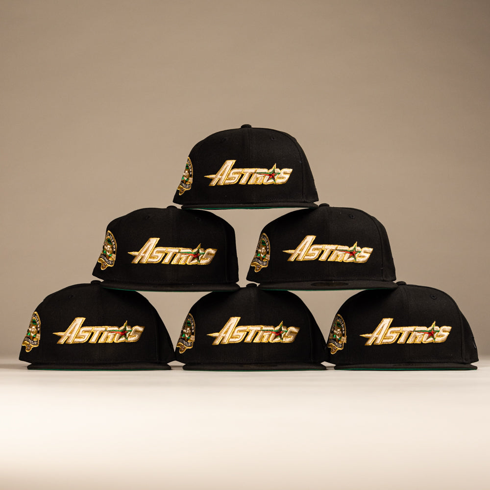 Six La Morenita Black 45th Houston Astros New Era 5950 Fitted hats with gold lettering are arranged in a pyramid on a neutral background, each featuring a colorful embroidered Mother of Guadalupe patch on the side.